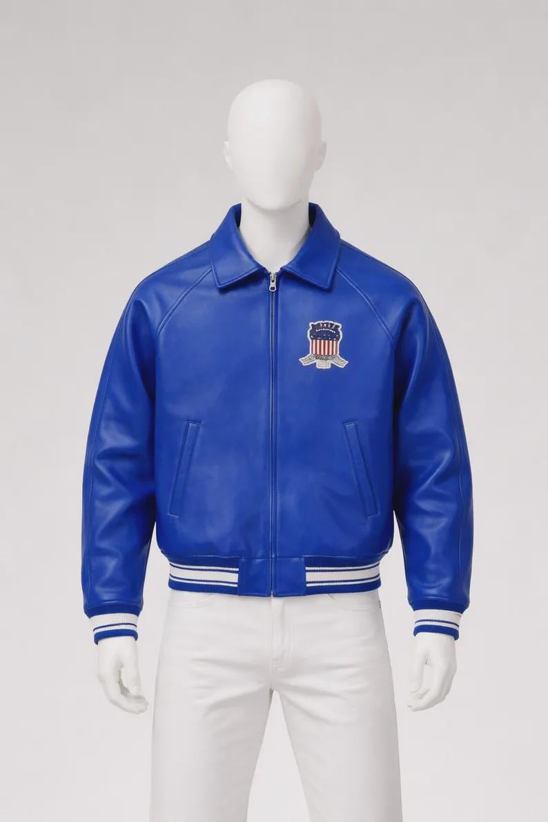 May include: A vibrant blue leather jacket with a zip-up front, a collared neckline, and a white and blue striped hem and cuffs. The jacket features a crest patch on the chest. The jacket is displayed on a mannequin.