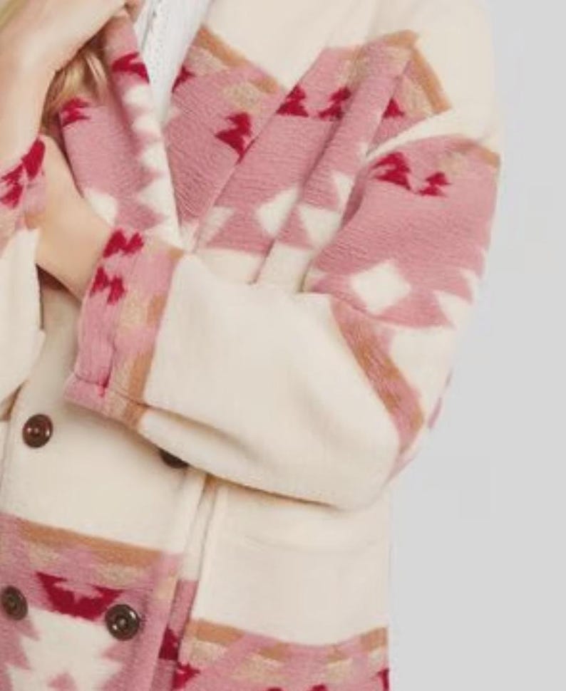 May include: Cream-colored coat with a geometric pattern in shades of pink, red, and brown. The coat features a double-breasted design with dark brown buttons. The sleeves and lapels showcase the patterned fabric.
