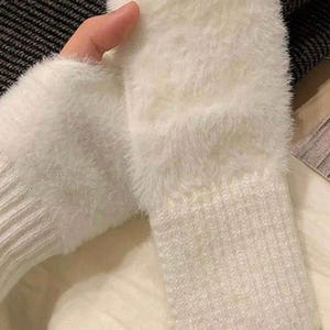May include: A pair of white, fluffy arm warmers. The arm warmers have a ribbed knit cuff and a soft, fuzzy upper section. The fabric appears to be a soft, warm material, perfect for cold weather. The arm warmers are a solid white color.