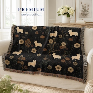 May include: A black woven cotton throw blanket featuring a repeating pattern of tan Corgi dogs and various brown and tan flowers. The blanket has fringed edges on the sides and includes the text PREMIUM woven cotton printed at the top.