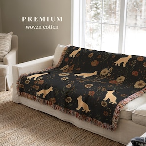 May include: A black woven cotton throw blanket featuring a repeating pattern of light tan dogs and various brown and orange flowers. The blanket has a fringed edge and displays the text PREMIUM woven cotton in the upper left corner.