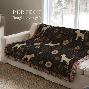 May include: A black woven throw blanket featuring a repeating pattern of light tan beagle silhouettes and various brown and orange floral motifs. The blanket has a fringed edge and includes the text "PERFECT Beagle lover gift" at the top.