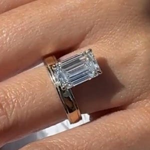 May include: A gold and silver engagement ring with a large, rectangular, clear gemstone. The ring is on a finger, with the band showing a two-tone design. The setting is a classic, elegant style, perfect for a special occasion.