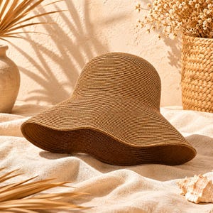 May include: A brown, wide-brimmed sun hat with a wavy edge. The hat is made of woven material and sits on a sandy surface. The hat is designed to provide shade from the sun.