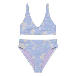 Puede incluir: Conjunto de bikini de dos piezas con un estampado floral azul claro sobre un fondo crema. La parte superior tiene un diseño de cuello en V, y la parte inferior de cintura alta tiene un interior lila claro. El diseño floral incluye pequeños acentos verdes.