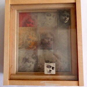 May include: A wooden frame with a glass front containing a collage of images of faces. The images are in black and white and sepia tones. The frame has a red knob on the top.
