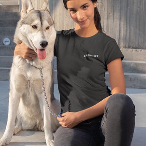 Könnte beinhalten: Ein schwarzes T-Shirt mit dem weißen Text "CREW LIFE". Eine Frau trägt das Shirt und sitzt neben einem grau-weißen Siberian Husky-Hund. Der Hund ist an der Leine.