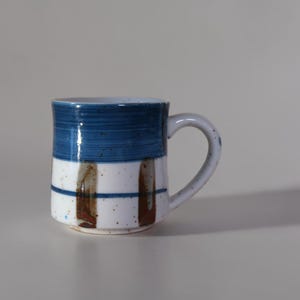 Taza de gres vintage con banda azul y esmalte moteado, estilo rústico de cerámica.