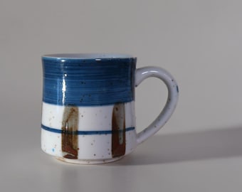 Taza de gres vintage con banda azul y esmalte moteado, estilo rústico de cerámica.