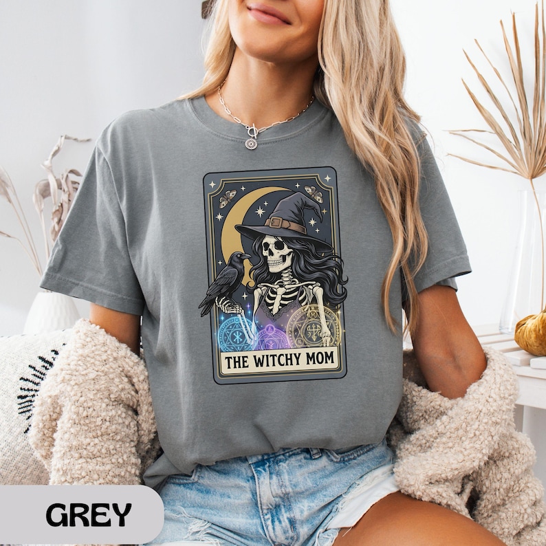 Woman wearing grey t-shirt with witchy skeleton graphic and text.