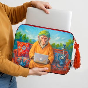 May include: A laptop sleeve featuring a colorful illustration of a monkey wearing a turban and robe, holding a laptop. The sleeve has a red zipper and a decorative orange tassel. The artwork includes a hookah and ornate cushions.