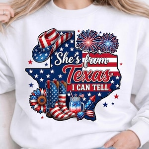 Op de afbeelding: Een wit sweatshirt met een afbeelding van de staat Texas in Amerikaanse vlagpatronen, een cowboyhoed, cowboylaarzen, een zonnebloem, vuurwerk, een glazen pot en een zonnebril. De tekst luidt, She's from Texas I CAN TELL.