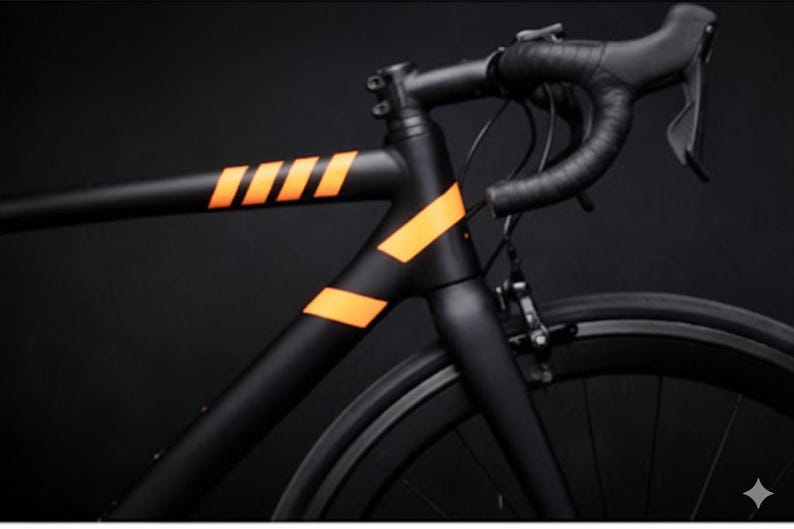 May include: A sleek black road bike with orange accent stripes on the frame. The handlebars are wrapped in black tape, and the tires are black. The bike is set against a dark background.