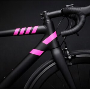 May include: A black road bicycle with pink accents. The frame is matte black with bright pink stripes and angled accents. The handlebars and tires are black, set against a dark background.