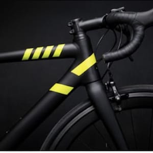 May include: A black road bicycle with yellow accents. The bicycle frame is matte black with bright yellow stripes and angled accents. The handlebars are wrapped in black tape, and the wheels are black.