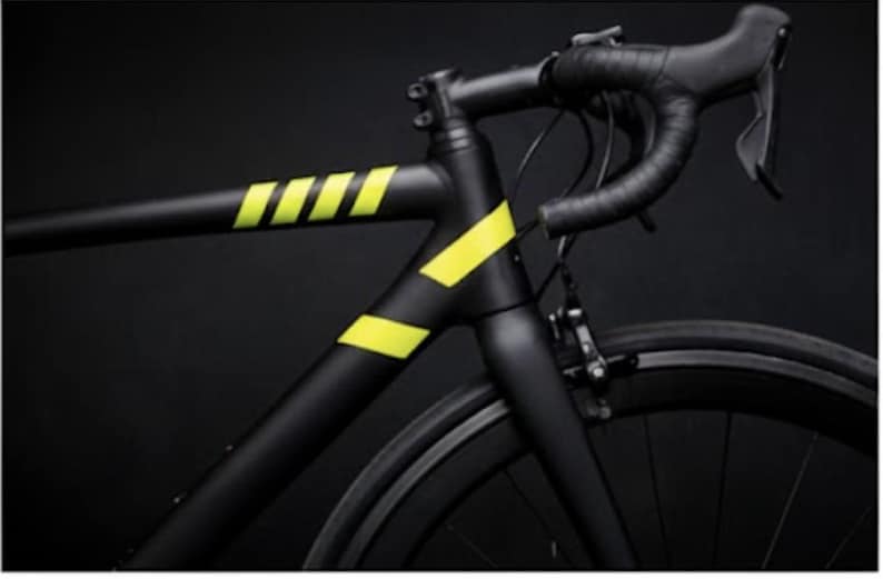 May include: A black road bicycle with yellow accents. The bicycle frame is matte black with bright yellow stripes and angled accents. The handlebars are wrapped in black tape, and the wheels are black.