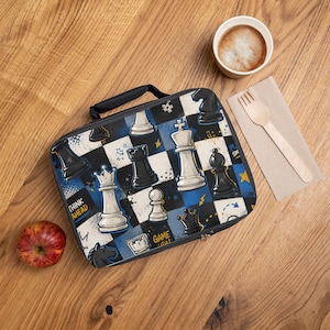 May include: A rectangular lunch bag featuring a black and blue checkered pattern with white and black chess piece illustrations, including kings, queens, and rooks. The design includes yellow stars, lightning bolts, and the text "THINK AHEAD" and "GAME ON".