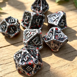 Könnte beinhalten: Set aus sieben metallischen Würfeln mit Steampunk-Ästhetik. Die Würfel sind silberfarben mit schwarzen und roten Akzenten, mit komplizierten mechanischen Designs und Zahlen. Die Würfel sind auf einer Holzoberfläche angeordnet.