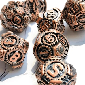 Könnte beinhalten: Eine Sammlung kupferfarbener Würfel im Steampunk-Stil. Jeder Würfel weist komplizierte Zahnrad- und Zahnkranzdesigns auf, mit Zahlen auf verschiedenen Seiten. Die Würfel sind auf einer weißen Oberfläche angeordnet und zeigen ihre detaillierte Handwerkskunst.