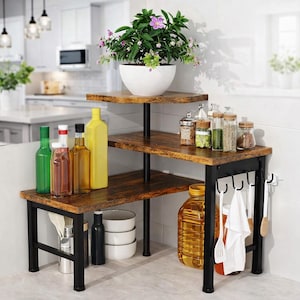 May include: A three-tiered corner shelf with a rustic wood finish and black metal frame. The top shelf holds a white pot with a flowering plant. Various bottles, jars, and kitchen utensils are displayed on the shelves.