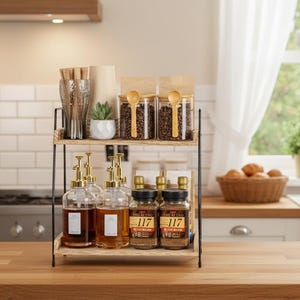 Puede incluir: Un estante de cocina de dos niveles de madera y metal que muestra granos de café, siropes y especias. Se ven botellas de vidrio transparente con boquillas doradas y frascos con el texto "117". Una cafetera y una tetera están en el fondo.