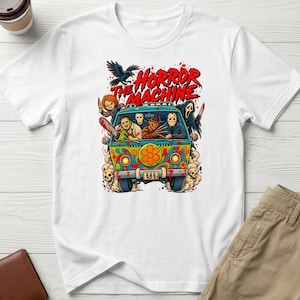 May include: A white short-sleeve t-shirt featuring a colourful graphic of a psychedelic van filled with horror movie characters. The text "THE HORROR MACHINE" is printed above the van, which has a license plate reading "666" and blood splatters.
