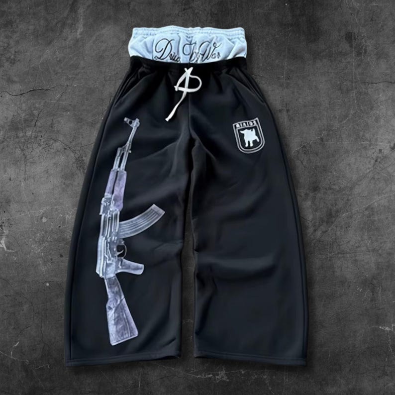 May include: Black sweatpants with a white drawstring and a light blue waistband. The left leg features a graphic of a transparent AK-47 rifle. A white emblem with a bull is on the right leg. The waistband has the text "D.W.S."