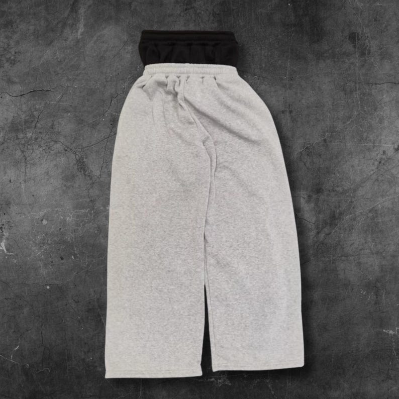 May include: A pair of gray sweatpants with a black waistband. The pants have a drawstring and a split at the bottom of the legs. The fabric appears to be a soft, comfortable material.