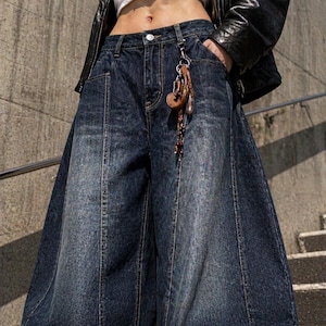 Pode incluir: Jeans de ganga azul escuro de perna larga, cintura alta e um detalhe de costura &uacute;nico na frente. Os jeans apresentam um porta-chaves decorativo preso &agrave; presilha. A ganga tem um aspeto desbotado.