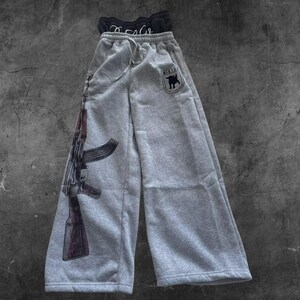 May include: Gray sweatpants with a drawstring waist and a large graphic of an AK-47 rifle on the left leg. The right leg features a small patch with a bull graphic and the text "H1R10". A black top is visible at the top.