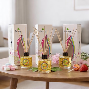 Puede incluir: Tres difusores de aromaterapia de vidrio con varillas de madera y la palabra "Armony" en la etiqueta. Los difusores están sobre una mesa de madera con una fresa, una piruleta y caramelos de colores. Las cajas detrás de los difusores también tienen la palabra "Armony".
