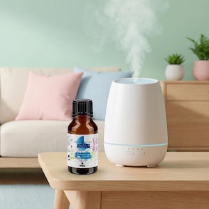 Puede incluir: Un difusor de aceites esenciales blanco con una luz azul y una botella de vidrio marrón de aceite esencial etiquetada como "ACUARIO" sobre una mesa de madera. El difusor emite una corriente de vapor. El fondo incluye un sofá con cojines rosas y azules.