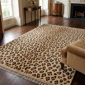 May include: A rectangular area rug featuring a repeating leopard print pattern in shades of tan, brown, and black. The rug has a short pile texture and is finished with a fringe trim along the two shorter edges, lying flat on a dark wood floor.