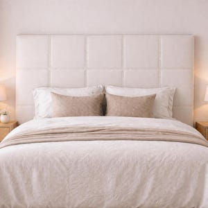 Peut inclure: Un lit avec une tête de lit blanche matelassée et des coutures décoratives. Le lit est fait de linge blanc et comprend deux coussins rectangulaires beiges. Une couverture beige est drapée sur le lit. Des lampes de chevet sont visibles.