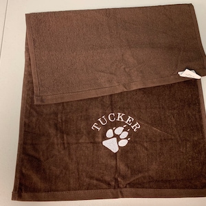 May include: Brown towel with white embroidery of a paw print and the name "TUCKER".
