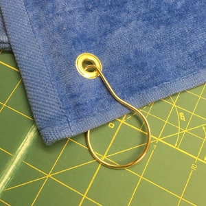 May include: A blue towel with a gold metal grommet and a gold metal ring attached.