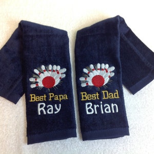 May include: Two navy blue towels with embroidered bowling pins and a ball. The towels have the text "Best Papa Ray" and "Best Dad Brian" embroidered on them.