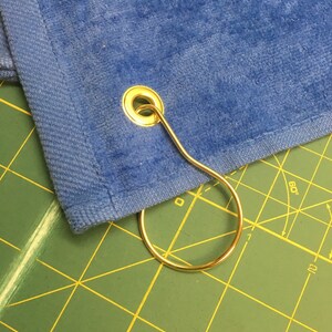 May include: A blue towel with a gold metal grommet and a gold metal ring attached.