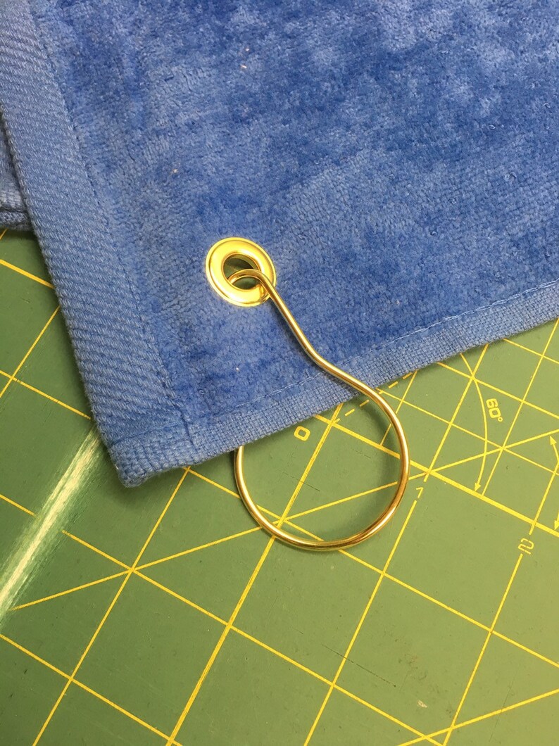 May include: A blue towel with a gold metal grommet and a gold metal ring attached.