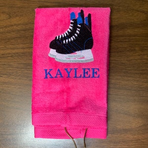 May include: Pink towel with a gold hook, embroidered with a pair of black ice skates and the name "KAYLEE".