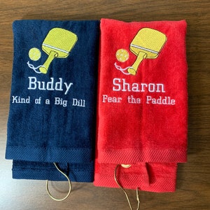 May include: Two personalised towels with embroidered paddleball rackets and text. The blue towel says "Buddy Kind of a Big Dill" and the red towel says "Sharon Fear the Paddle".