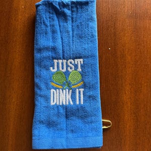 May include: Blue towel with the text "JUST DINK IT" embroidered in white with two green and yellow pickleball paddles.