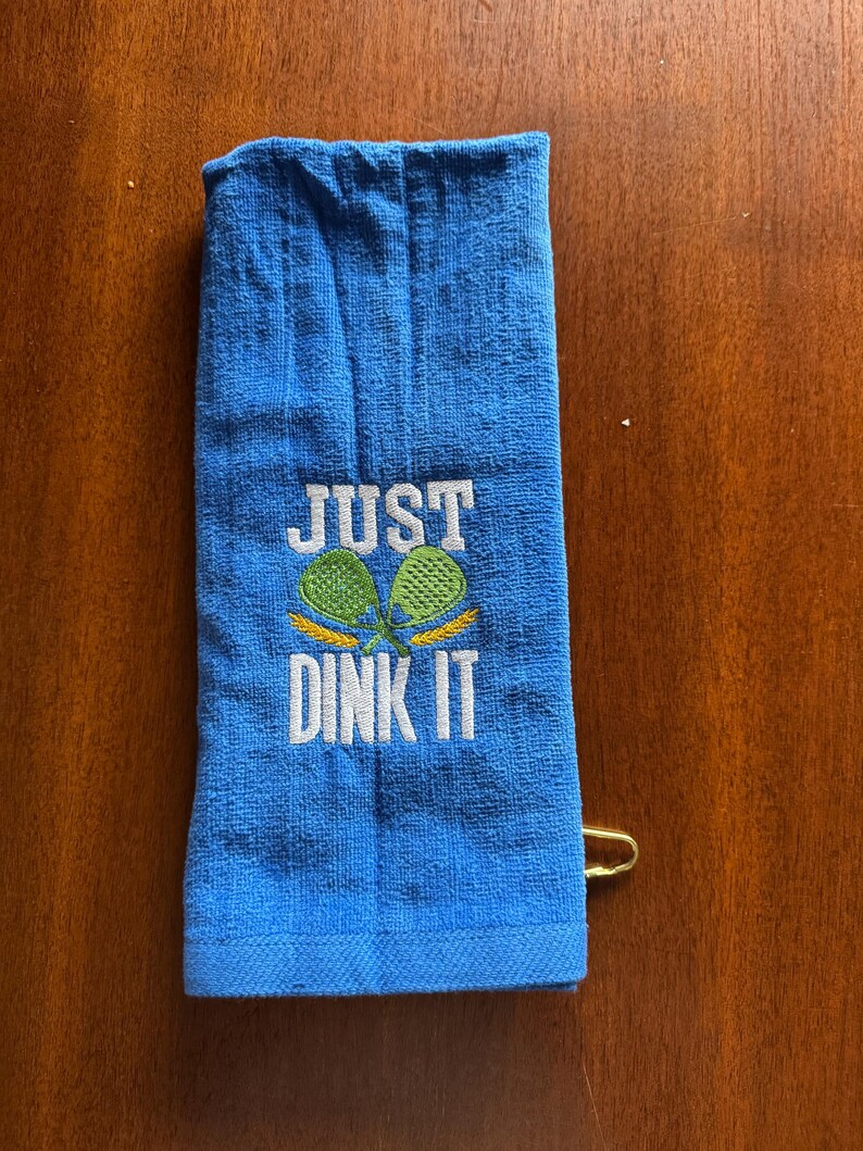 May include: Blue towel with the text "JUST DINK IT" embroidered in white with two green and yellow pickleball paddles.