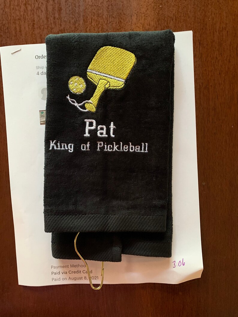May include: Black towel with embroidered yellow pickleball paddle and ball, and the text "Pat King of Pickleball".