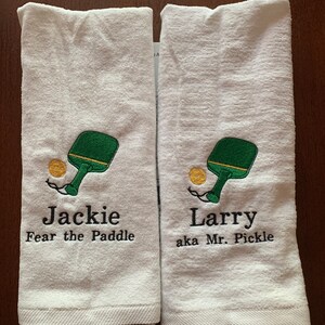 May include: Two white towels with embroidered paddleball designs and personalized text. The first towel says "Jackie Fear the Paddle" and the second towel says "Larry aka Mr. Pickle".