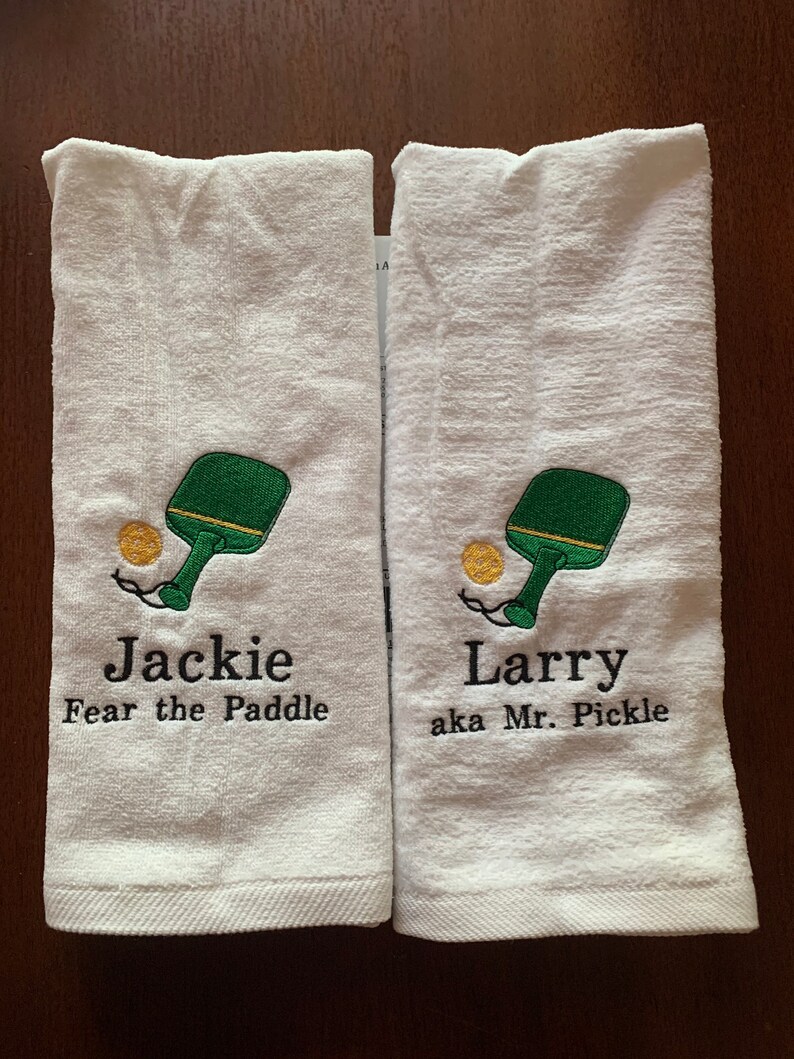 May include: Two white towels with embroidered paddleball designs and personalized text. The first towel says "Jackie Fear the Paddle" and the second towel says "Larry aka Mr. Pickle".