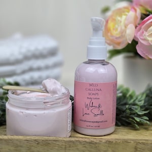 May include: A jar and bottle of pink body lotion are displayed on a wooden tray. The bottle has a pump dispenser and a pink label with the text "Wishes & Love Spells". The jar contains a scoop of lotion. A bouquet of pink flowers is in the background.