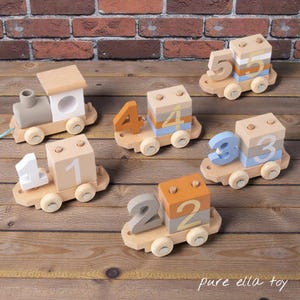Puede incluir: Juego de seis trenes de juguete de madera. Cada vagón muestra un número del 1 al 5, con una locomotora. Los vagones están pintados en tonos neutros con un acabado de madera natural. Juguete para niños.