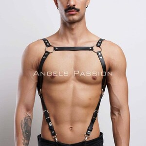May include: Black leather body harness with silver-tone metal rings and hardware. The harness features adjustable straps and the text "ANGELS PASSION". This accessory is designed to be worn over the torso.