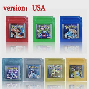 Puede incluir: Una colección de siete cartuchos de Pokémon para Game Boy de colores. Los cartuchos son rojos, verdes, azules, celeste, grises, amarillo verdoso y amarillos. Cada cartucho presenta un personaje Pokémon con el texto "Pokémon" y "THIS SIDE OUT". El texto "version: USA" está en la parte superior.